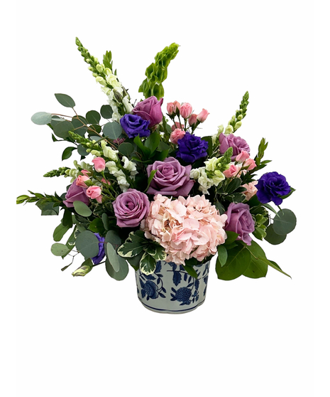 An arrangement of pink hydrangeas, lavender roses, purple lisiathus, white snapdragons and pink spray roses in a blue and white ceramic vase